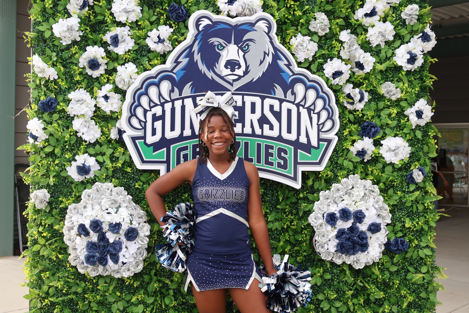 Gunderson Grizzlies cheerleader in front of the floral greenery wall