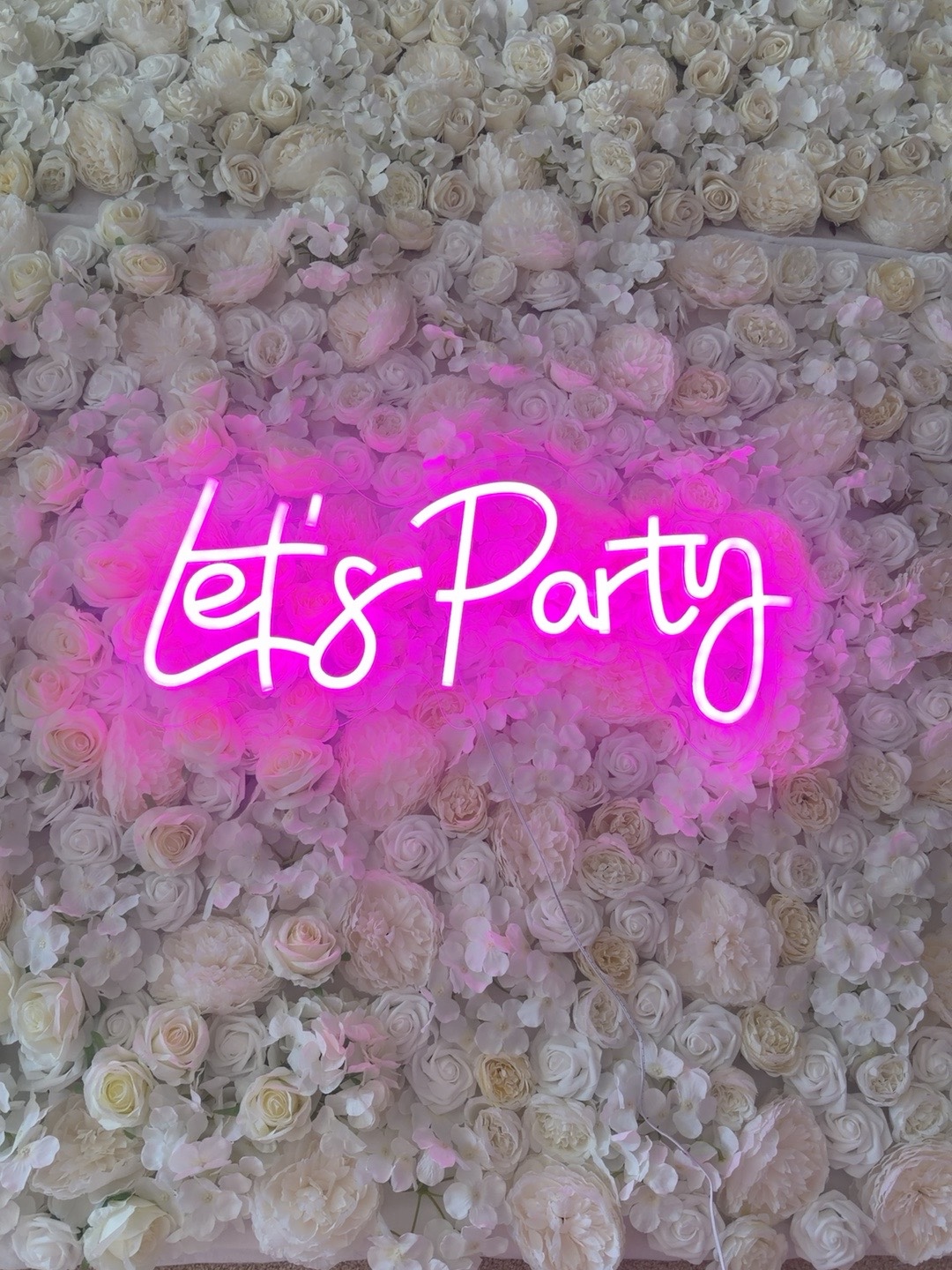 Let's Party pink neon sign on white flower wall